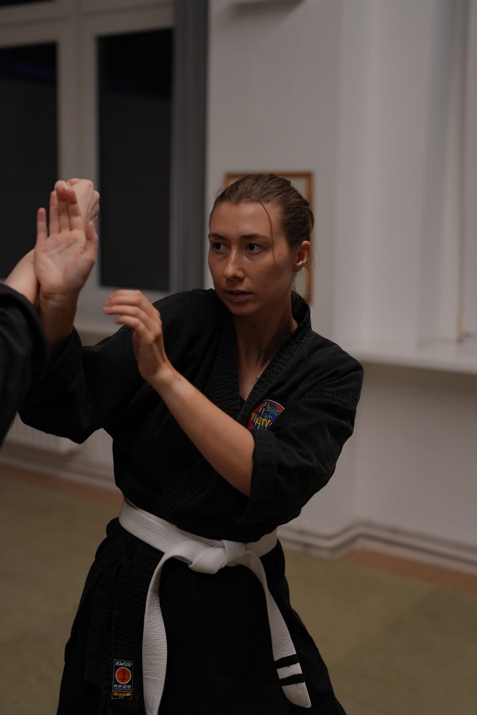Victoria in a black martial arts uniform and white belt, hands raised in a guard stance.