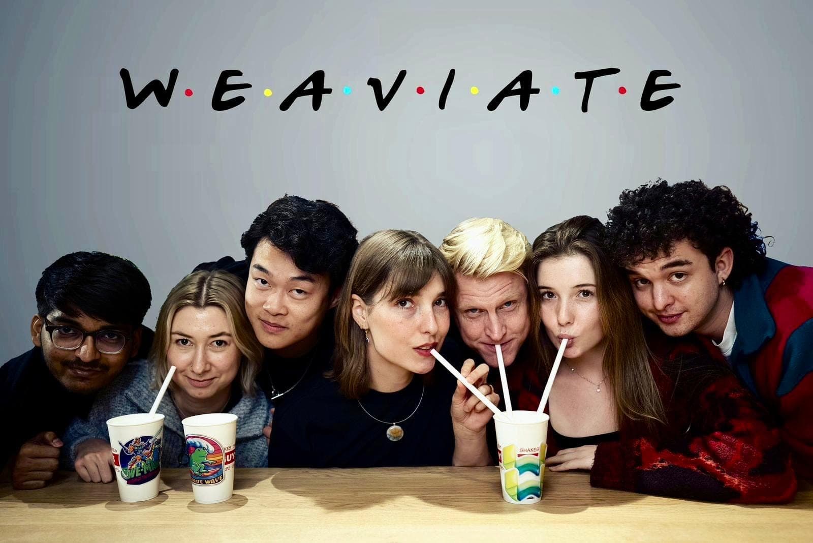 Seven Weaviate colleagues leaning together over milkshakes beneath a sign reading WEAVIATE in the Friends typeface.